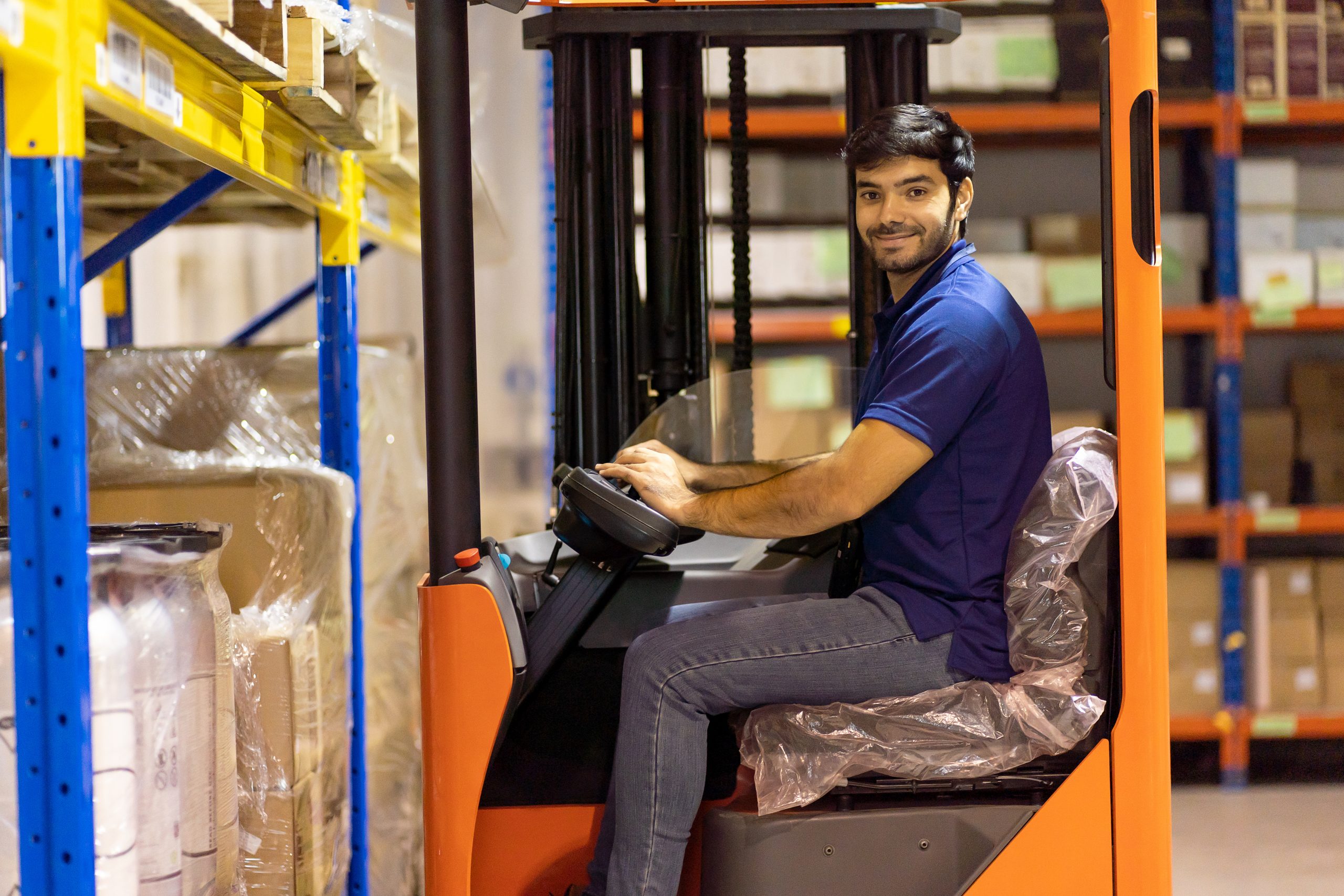 Male warehouse worker driving and operating on forklift truck fo